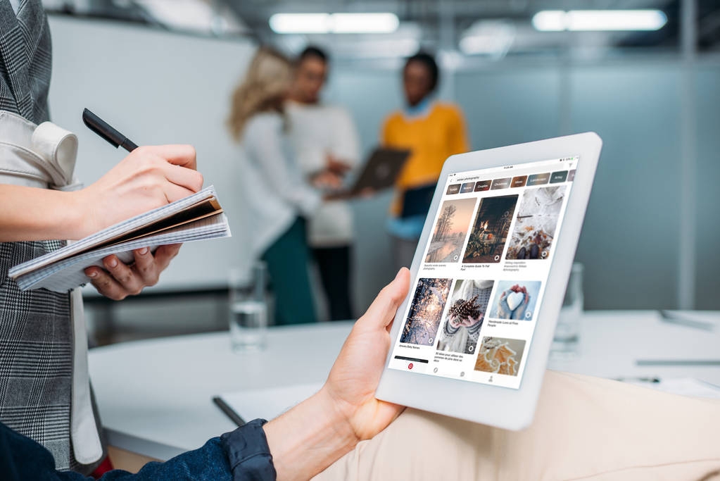 商人手持平板电脑 pinterest 在现代办公室的屏幕上, 而同事做笔记