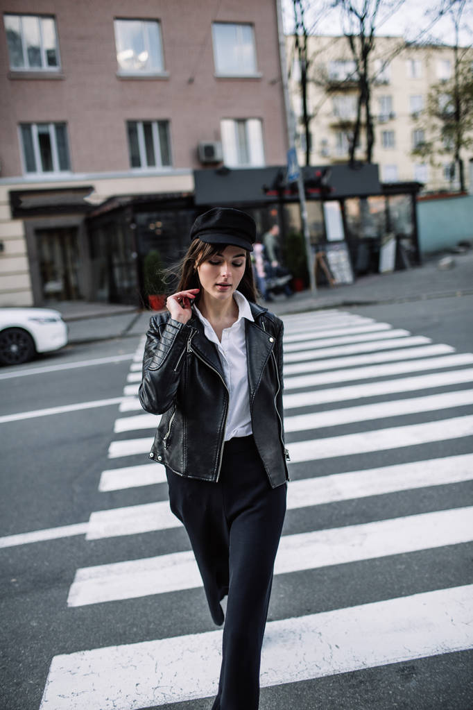 美丽的女孩与太阳镜。一个模型在一个时髦的宽边帽子在一个行人过路处。在灰色色调和谐类似的衣服。街头风格射击。女性时尚.